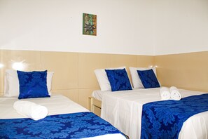 Una habitación de hotel con dos camas, cada una con ropa de cama azul y blanca, y un pequeño cuadro en la pared.