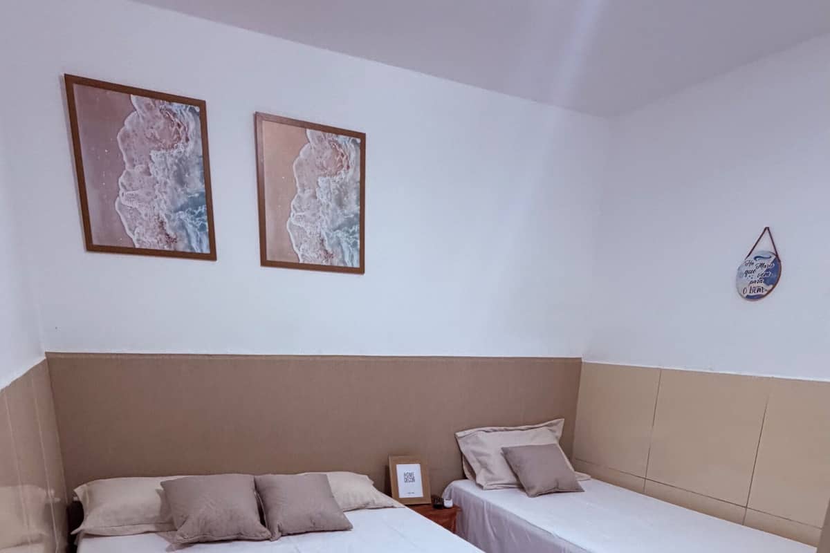 A hotel room with two beds, white bedding, a framed picture on the wall, and a small table with a sign.