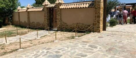 A stone wall with a gate, leading to a paved area with a stone pattern.