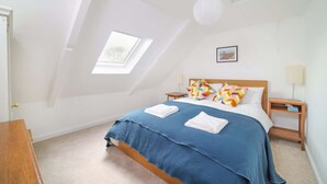 A bedroom with a sloped ceiling, a skylight, a bed with blue bedding, two nightstands, and a wooden dresser. - Beautiful Cottage & Garden, Quantock Hills (Bridgwater)