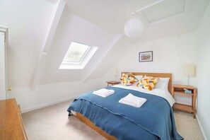 A bedroom with a sloped ceiling, a skylight, a bed with blue bedding, two nightstands, and a wooden dresser. - Beautiful Cottage & Garden, Quantock Hills (Bridgwater)