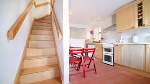 A kitchen with wooden cabinets, a red table, and a staircase. - Beautiful Cottage & Garden, Quantock Hills (Bridgwater)
