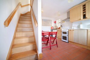 A kitchen with wooden cabinets, a red table, and a staircase. - Beautiful Cottage & Garden, Quantock Hills (Bridgwater)