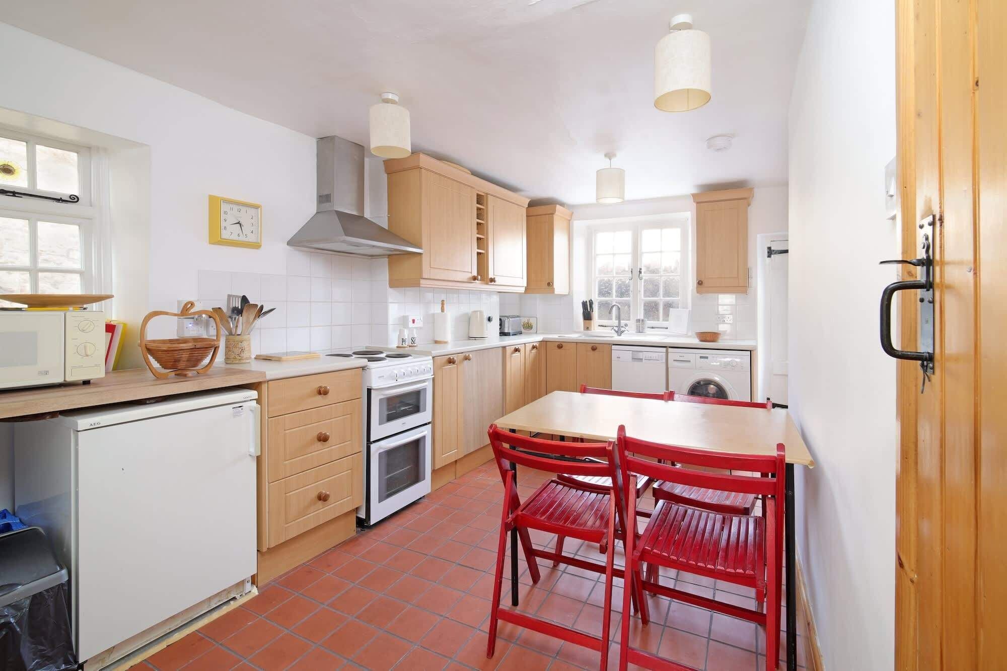 Une cuisine de taille réduite avec des meubles en bois, un poêle blanc, une table à manger rouge et une chaise rouge.