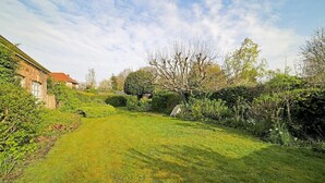 A well-maintained garden with a lawn, various shrubs, and a building with a red roof.