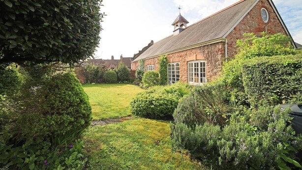 A stone building with a steep roof, surrounded by well-maintained hedges and a grassy lawn.