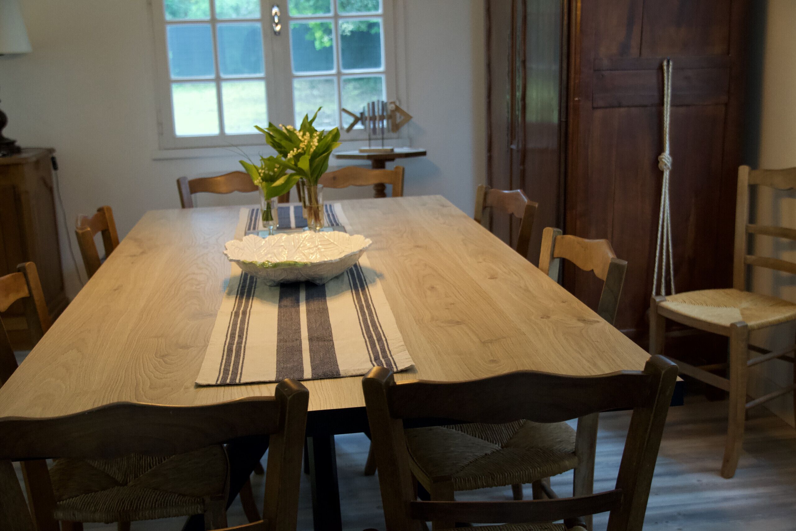Ein Holztisch mit einem Blumenstrauß, gestreifte Platzsets und mehreren Holzstühlen.