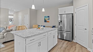 A modern kitchen with white cabinets, a granite countertop, stainless steel appliances, and pendant lighting.