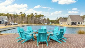 A patio with a brick floor, a pool, and turquoise Adirondack chairs.