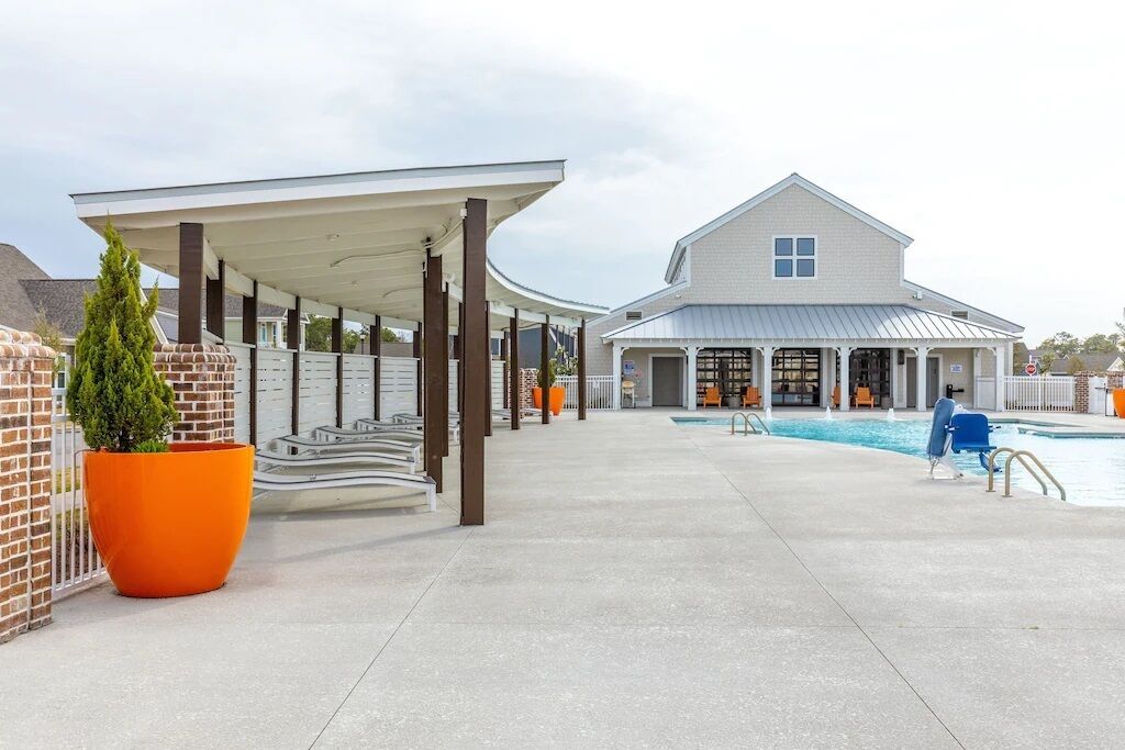 A covered outdoor area with a pool, a building with a white facade, and a brick wall.