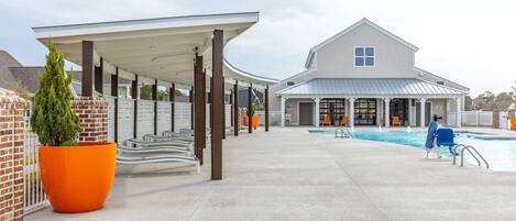 A covered outdoor area with a pool, a building with a white facade, and a brick wall.