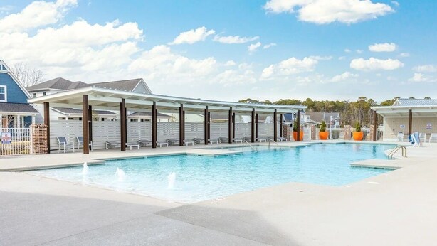 A swimming pool with a covered seating area, a fenced patio, and a clear sky.