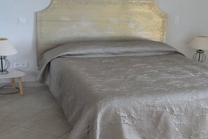 A bed with a textured headboard and a grey bedspread in a room with a tiled floor.