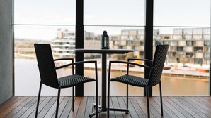 Ein Balkon mit zwei Stühlen und einem Tisch, mit Blick auf ein Gewässer und Gebäude.