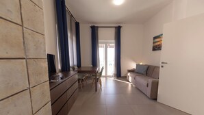 Ein modernes Wohnzimmer mit einer Couch, einem Esstisch mit Stühlen und einem Fernseher auf einem Schrank.