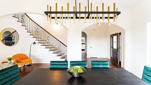 A modern dining area with a dark wooden table, teal upholstered chairs, and a central bowl of green salad. - Relax & Play in Style: Luxury Home w/ Infinity Pool, Game Room & Alfresco Dining (Jonestown)