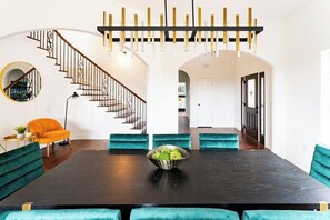 A modern dining area with a dark wooden table, teal upholstered chairs, and a central bowl of green salad. - Relax & Play in Style: Luxury Home w/ Infinity Pool, Game Room & Alfresco Dining (Jonestown)