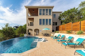 A modern two-story house with a swimming pool, outdoor seating, and a wooden fence.