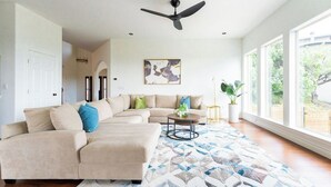 A living room with a sectional sofa, a ceiling fan, a large window, and a floor-to-ceiling view. - Relax & Play in Style: Luxury Home w/ Infinity Pool, Game Room & Alfresco Dining (Jonestown)