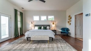 A bedroom with a bed, bedside lamps, a bench, a chair, and a ceiling fan. - Relax & Play in Style: Luxury Home w/ Infinity Pool, Game Room & Alfresco Dining (Jonestown)