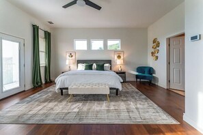A bedroom with a bed, bedside lamps, a bench, a chair, and a ceiling fan. - Relax & Play in Style: Luxury Home w/ Infinity Pool, Game Room & Alfresco Dining (Jonestown)