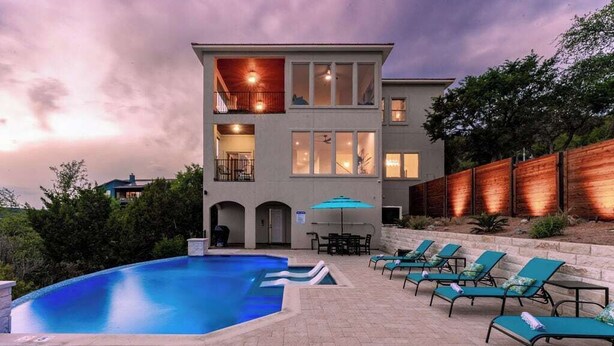 A modern two-story building with a swimming pool and outdoor seating. - Relax & Play in Style: Luxury Home w/ Infinity Pool, Game Room & Alfresco Dining (Jonestown)