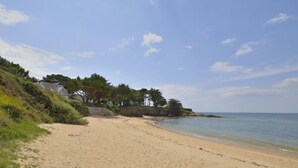 Ein sandiger Strand mit blauem Himmel, vereinzelten Wolken und ruhigem Meer.