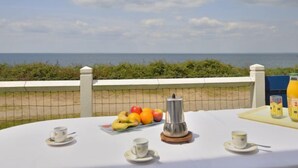 Ein Tisch ist reichhaltig mit Frühstück gedeckt, mit einer Kaffeekanne, und bietet Blick auf das Meer.