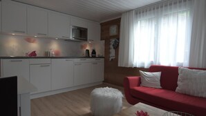 Une cuisine moderne avec des meubles blancs, un four à micro-ondes et un canapé rouge dans l’espace salon.
