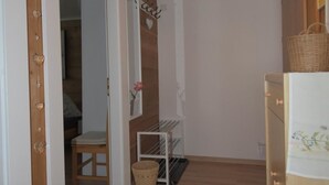Un couloir avec un plancher en bois, une porte blanche, une petite table avec un panier et une étagère fixée au mur.