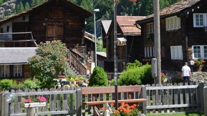 Un bâtiment traditionnel en bois, doté d’un toit à pente, entouré d’une clôture en bois et de parterres de fleurs.