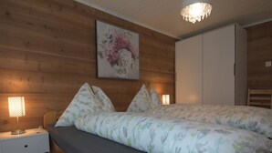 Une chambre à coucher avec une tête de lit en bois, un lit recouvert d’une literie à motifs floraux, une table de chevet avec une lampe et un tableau représentant des fleurs accroché au mur.