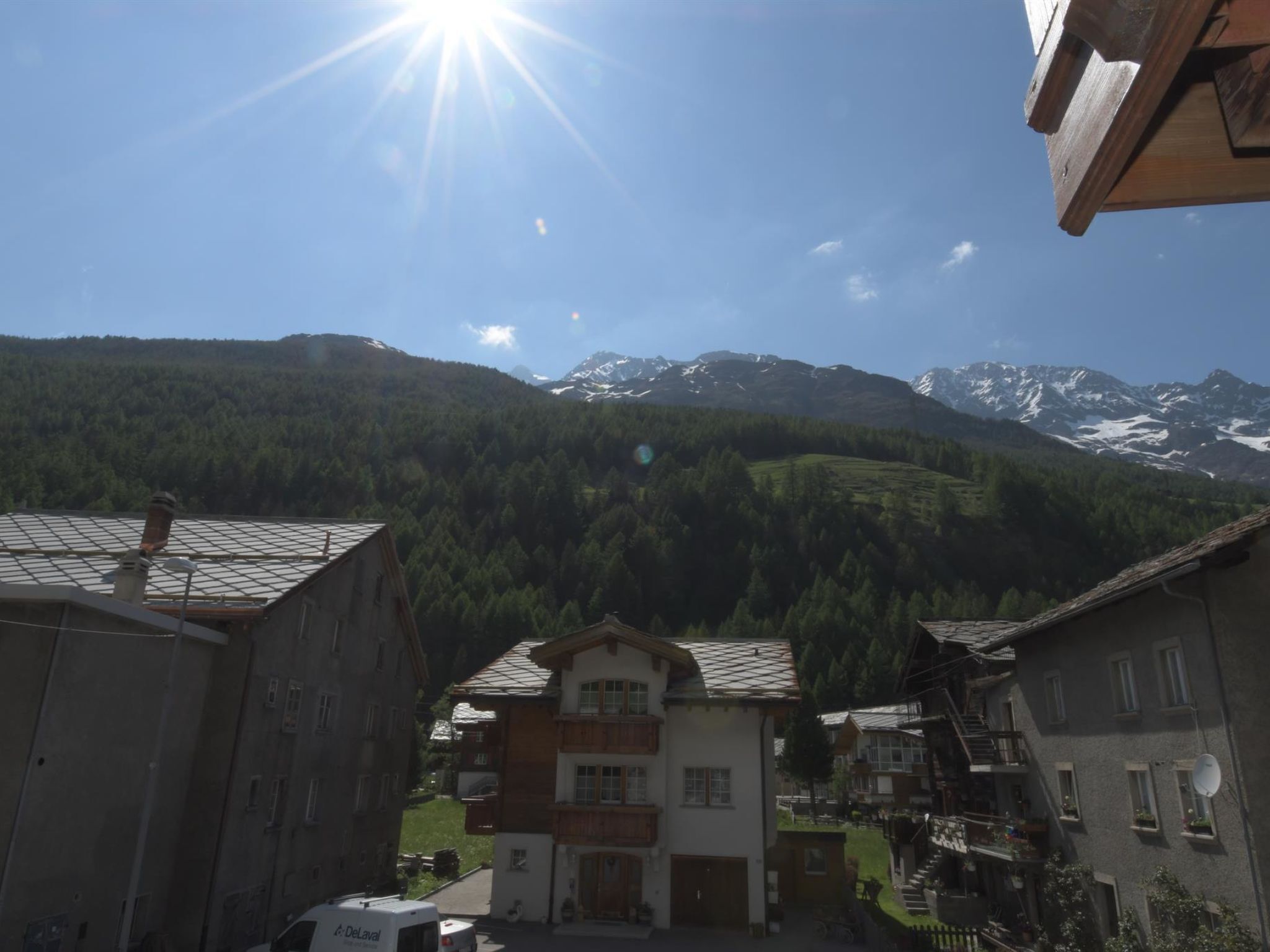 Un pueblo de montaña con edificios tradicionales, cielo despejado y picos nevados al fondo.