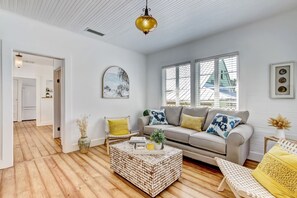 Uma sala de estar moderna com um sofá cinzento, uma poltrona branca, uma mesa de centro de madeira e uma luminária pendente dourada.