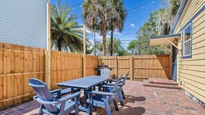 Un patio con tavolo e sedie in legno, una recinzione di legno e una casa con una porta blu.