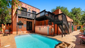 A pool area with a clear blue pool, a wooden deck, and a two-story building with balconies and decorative tiles. - The Gaudi House- Pool/Minutes to DNTN and Beach (St. Augustine)