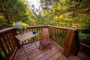 Una terraza de madera con una mesa y una silla, rodeada de un bosque.