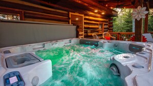 A hot tub with a control panel, surrounded by wooden deck furniture and a cabin-style interior. - Log Cabin Hot Tub Getaway (Walhonding)