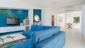 Un salon moderne avec un canapé d’angle bleu, un téléviseur à écran plat et un coin repas doté d’une table en verre.