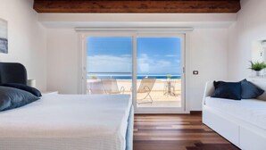 Une chambre dotée d’une grande porte-fenêtre coulissante donnant sur la plage, avec un lit, un canapé et un plafond en bois.