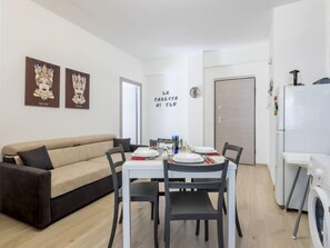 Un salon moderne avec un canapé beige, une table à manger dressée pour quatre personnes et un lave-linge.