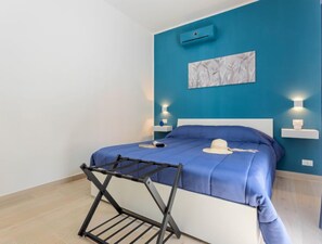 Une chambre à coucher avec une couvre-lit bleue, une tête de lit blanche et un climatiseur fixé au mur.