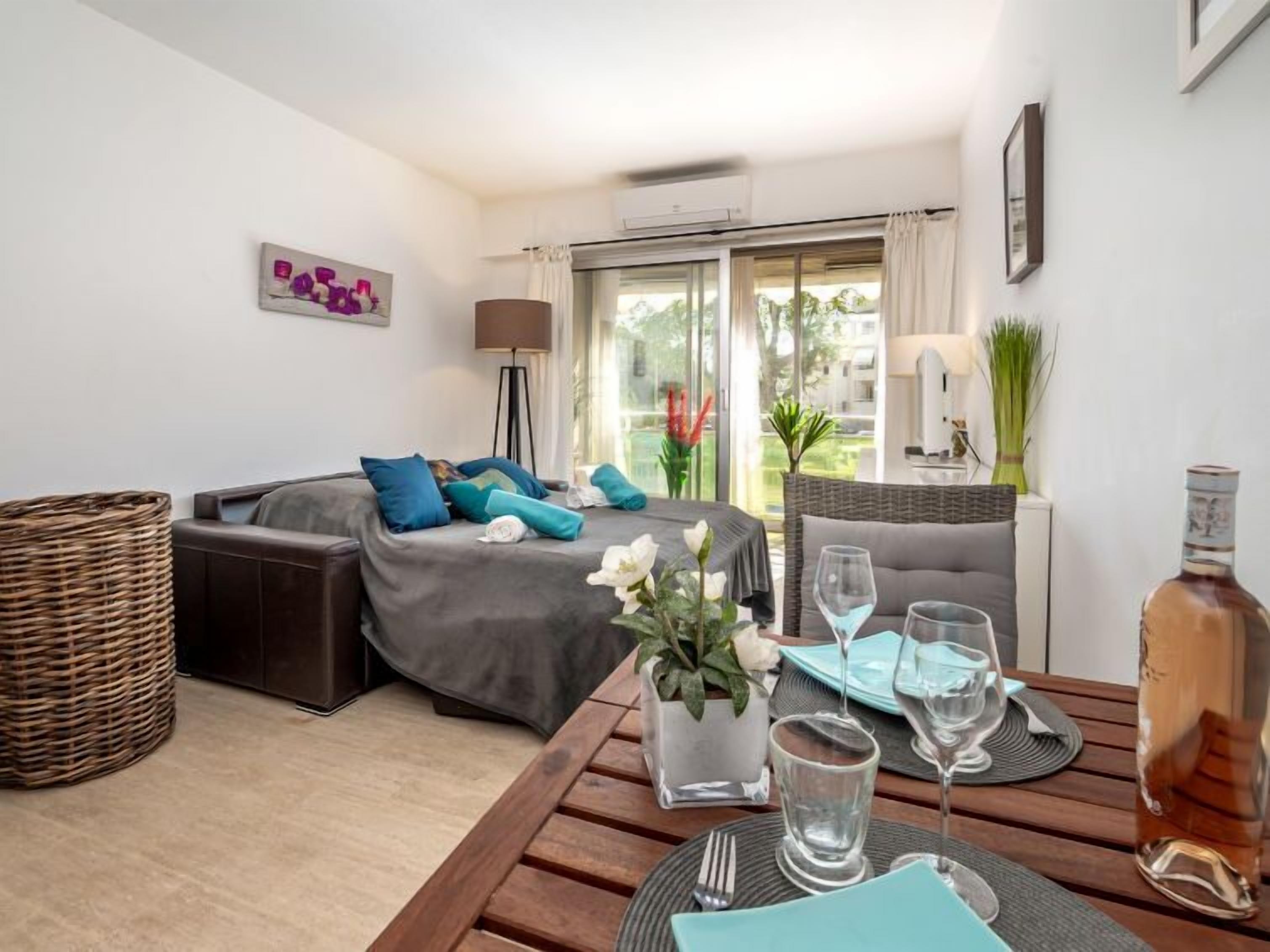 A modern hotel room with a sofa, a dining table set for two, and a large window with curtains.