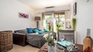 Ein modernes Hotelzimmer mit einer Couch, einem Esstisch für zwei Personen und einem großen Fenster mit Vorhängen.