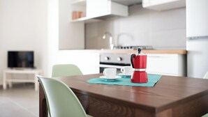 Une cuisine moderne avec des meubles blancs, une machine à café posée sur le plan de travail et un téléviseur en arrière-plan.