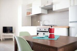 Une cuisine moderne avec des meubles blancs, une machine à café posée sur le plan de travail et un téléviseur en arrière-plan.