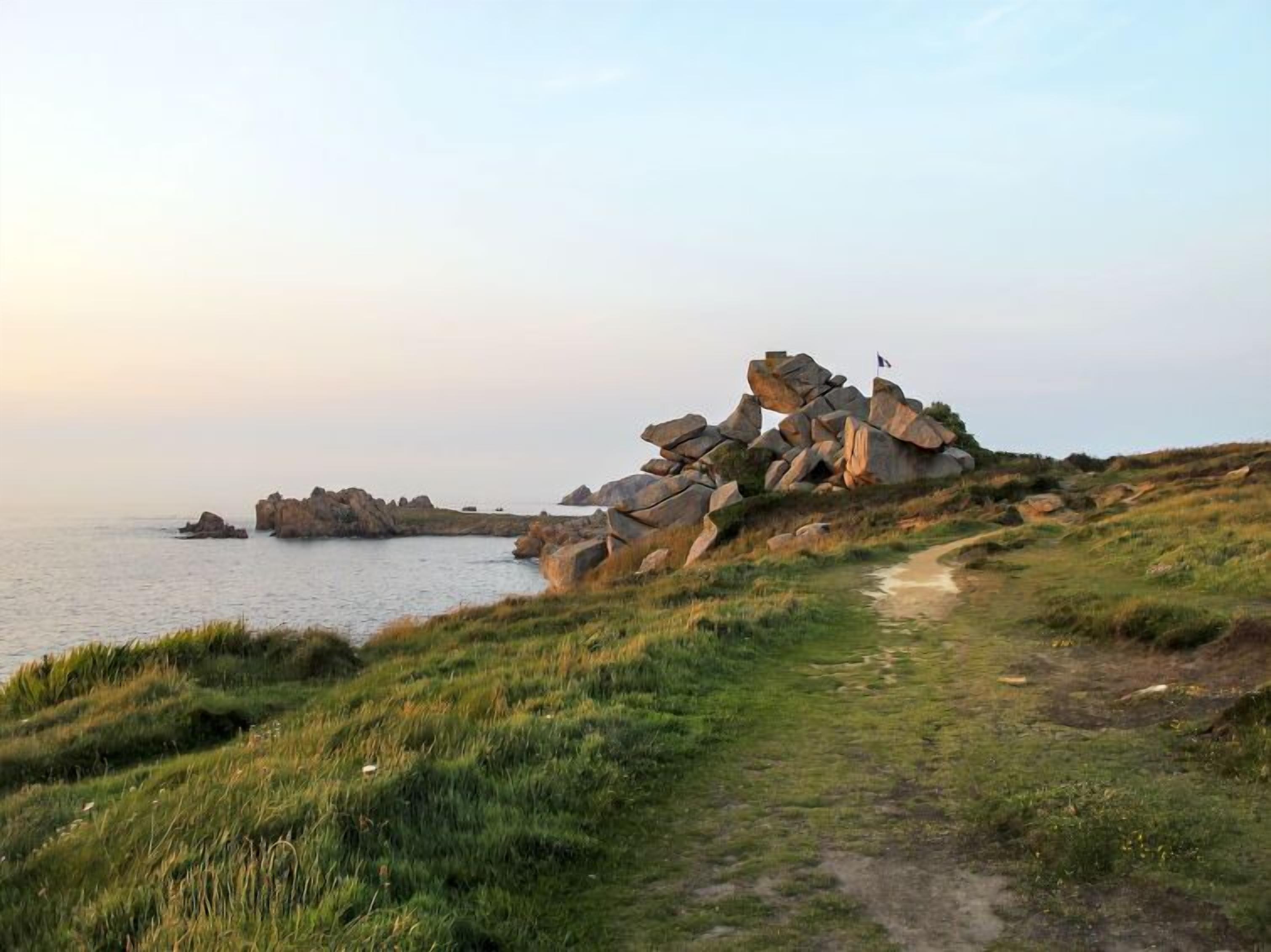 A coastal landscape with a rocky outcrop and a path leading to it.