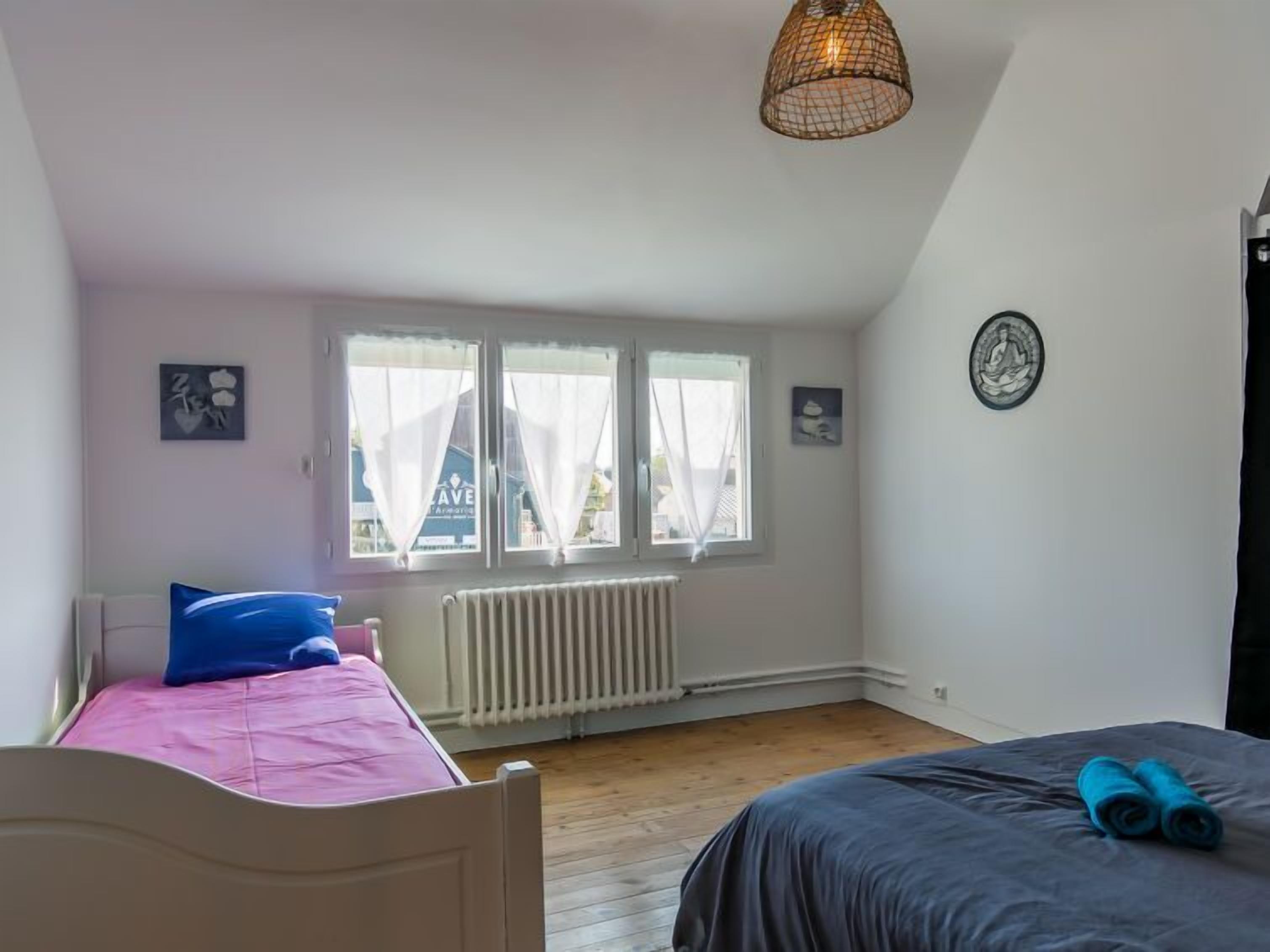 Ein Schlafzimmer mit einem Bett, einem Heizkörper, einem Fenster mit Vorhängen und einer Pendelleuchte.