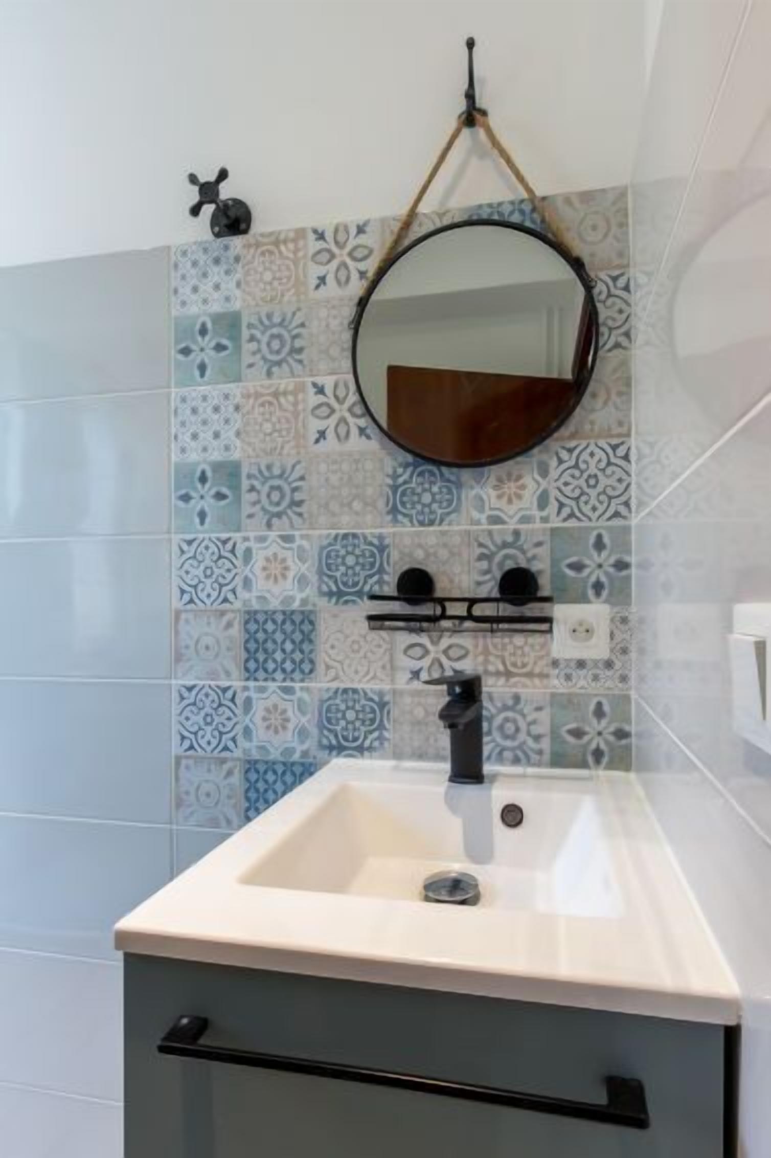 Une salle de bain avec un lavabo, un miroir et des carreaux décorés.