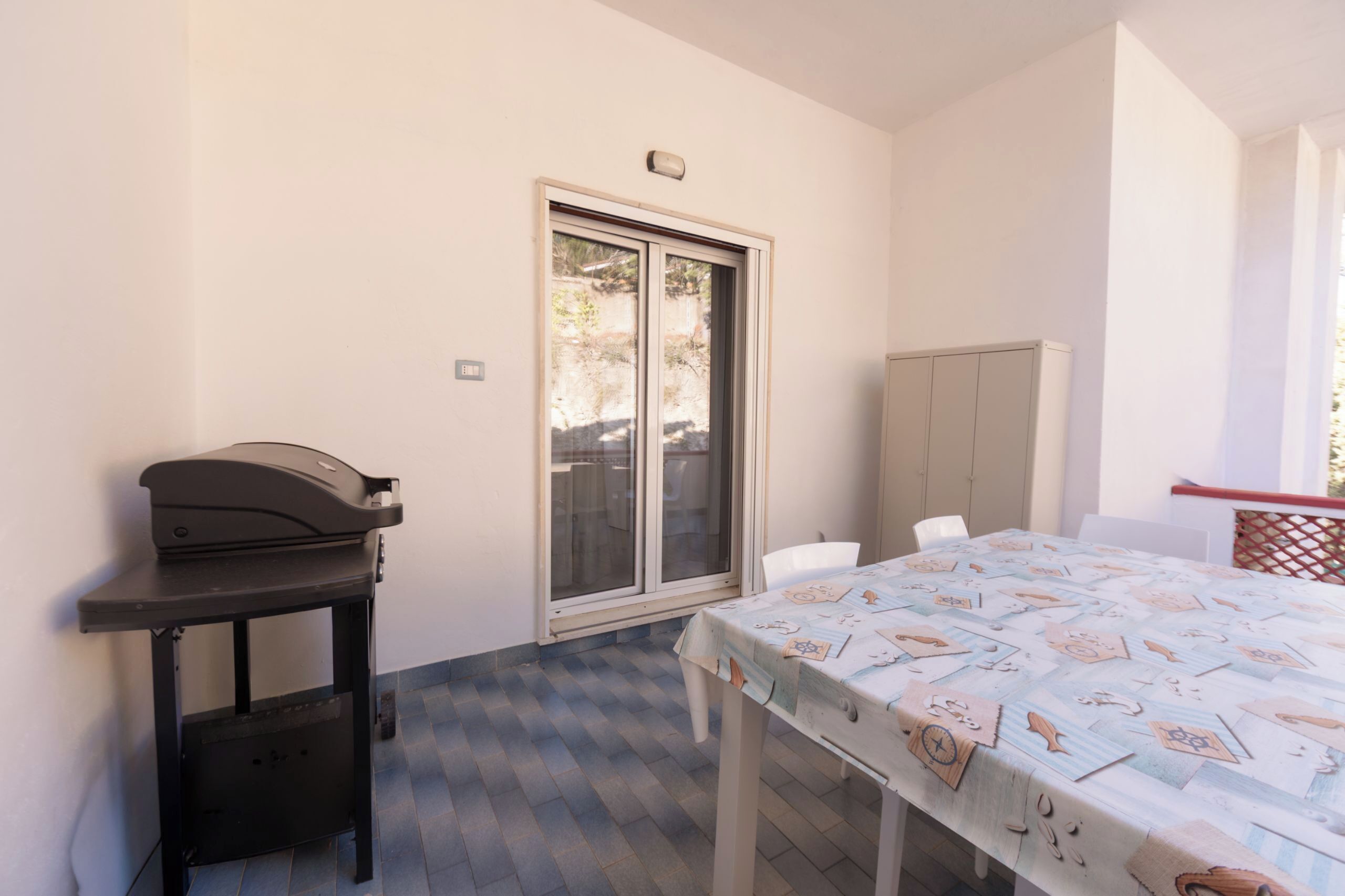 Une pièce avec une table recouverte d’une nappe à motifs variés, un barbecue sur la table et une porte-fenêtre coulissante donnant sur l’extérieur.